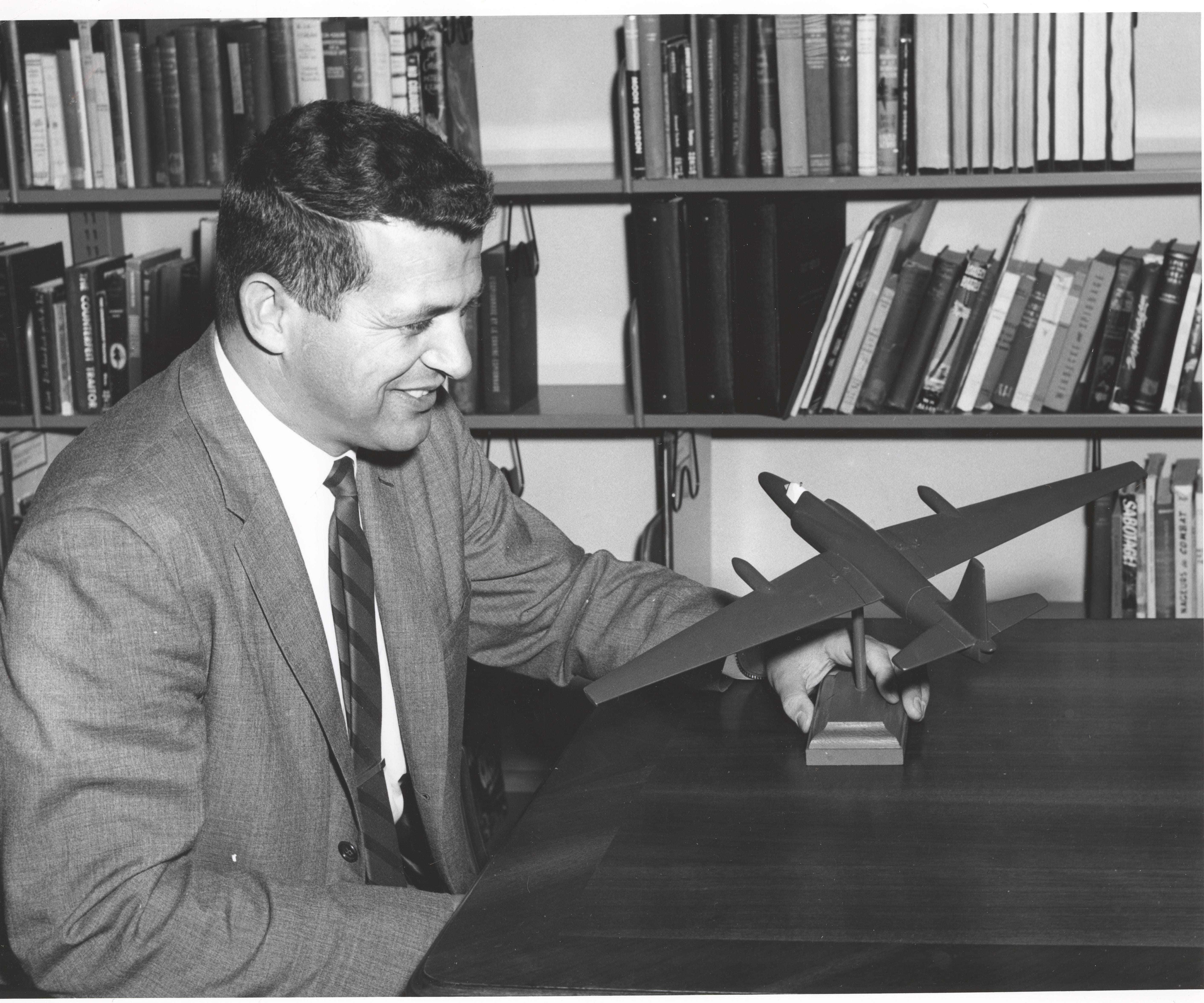 Francis Gary Powers holding a model plane in front of bookshelves.